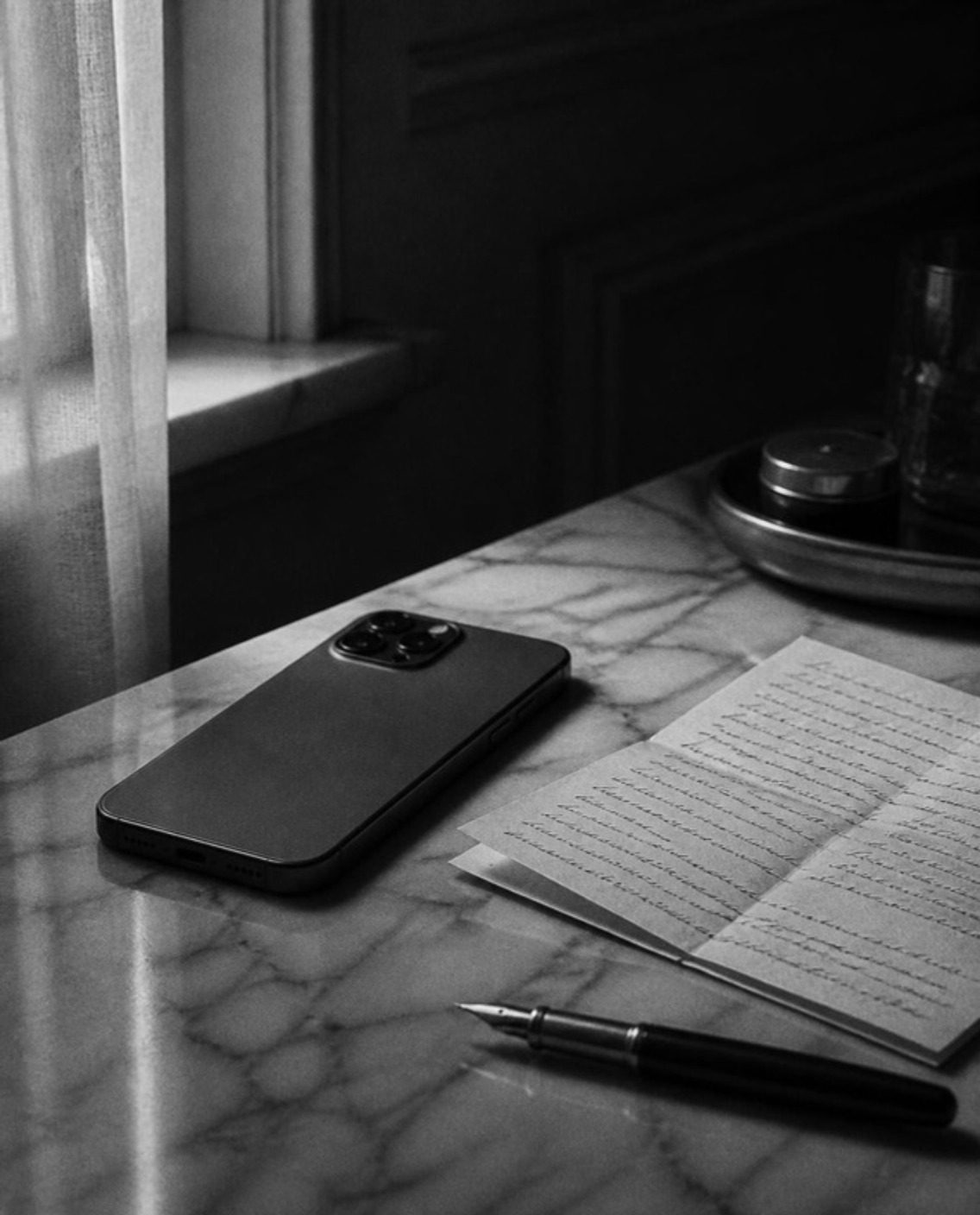 A phone face down on a marble table beside a fountain pen and a letter